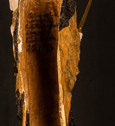 Zdjęcie nr 27: Rzeźba drążona ustawiona na niewielkim, wielobocznym postumencie. Maria ukazana w pozycji stojącej, frontalnie z ciałem ułożonym z lekkim kontrapoście. Lewą ręką podtrzymuje Dzieciątko Jezus, w prawej trzyma złocone berło zwieńczone kwiatem. Matka Boska przedstawiona jako młoda kobieta o podłużnej twarzy z wysokim czołem, migdałowatymi oczami oraz krótkim nosem i małymi ustami ułożonymi w delikatny uśmiech. Karnacja jasna, policzki wyraźnie zaróżowione. Długie, ciemne i falowane włosy rozdzielone przedziałkiem opadają na ramiona postaci. Na głowie Marii ciemna chusta oraz złocona korona (pozostałość korony?) lub diadem. Madonna jest ubrana w ciemną suknię z długimi rękawami dekorowaną motywem roślinnym oraz złocony płaszcz spięty pod szyją klamrą w kształcie kwiatu. Dzieciątko Jezus przedstawione w pozycji siedzącej z głową mocno pochyloną w bok i skrzyżowanymi stópkami. W ręku trzyma otwartą księgę. Twarz owalna, pulchna, ciemne oczy skierowane w lewo, usta w wyraźnym uśmiechu. Włosy, krótkie, falowane w kolorze brązowym. Dzieciątko jest ubrane w złoconą tkaninę udrapowaną wokół bioder. Figura polichromowana i częściowo złocona. Na odwrociu napis „Powtóre odzłocona / zarządem x(iędza) / Pawła Pomian Izdeb / skiego przez / Karol(a) Rośka / R(oku) P(ańskiego) 1853”.