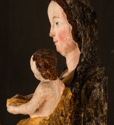 Zdjęcie nr 14: Rzeźba drążona ustawiona na niewielkim, wielobocznym postumencie. Maria ukazana w pozycji stojącej, frontalnie z ciałem ułożonym z lekkim kontrapoście. Lewą ręką podtrzymuje Dzieciątko Jezus, w prawej trzyma złocone berło zwieńczone kwiatem. Matka Boska przedstawiona jako młoda kobieta o podłużnej twarzy z wysokim czołem, migdałowatymi oczami oraz krótkim nosem i małymi ustami ułożonymi w delikatny uśmiech. Karnacja jasna, policzki wyraźnie zaróżowione. Długie, ciemne i falowane włosy rozdzielone przedziałkiem opadają na ramiona postaci. Na głowie Marii ciemna chusta oraz złocona korona (pozostałość korony?) lub diadem. Madonna jest ubrana w ciemną suknię z długimi rękawami dekorowaną motywem roślinnym oraz złocony płaszcz spięty pod szyją klamrą w kształcie kwiatu. Dzieciątko Jezus przedstawione w pozycji siedzącej z głową mocno pochyloną w bok i skrzyżowanymi stópkami. W ręku trzyma otwartą księgę. Twarz owalna, pulchna, ciemne oczy skierowane w lewo, usta w wyraźnym uśmiechu. Włosy, krótkie, falowane w kolorze brązowym. Dzieciątko jest ubrane w złoconą tkaninę udrapowaną wokół bioder. Figura polichromowana i częściowo złocona. Na odwrociu napis „Powtóre odzłocona / zarządem x(iędza) / Pawła Pomian Izdeb / skiego przez / Karol(a) Rośka / R(oku) P(ańskiego) 1853”.