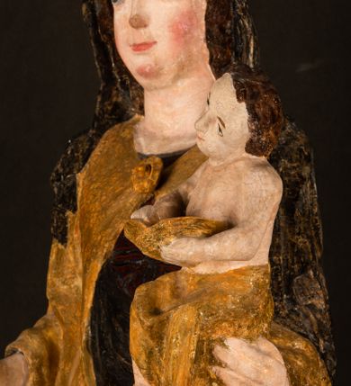 Zdjęcie nr 11: Rzeźba drążona ustawiona na niewielkim, wielobocznym postumencie. Maria ukazana w pozycji stojącej, frontalnie z ciałem ułożonym z lekkim kontrapoście. Lewą ręką podtrzymuje Dzieciątko Jezus, w prawej trzyma złocone berło zwieńczone kwiatem. Matka Boska przedstawiona jako młoda kobieta o podłużnej twarzy z wysokim czołem, migdałowatymi oczami oraz krótkim nosem i małymi ustami ułożonymi w delikatny uśmiech. Karnacja jasna, policzki wyraźnie zaróżowione. Długie, ciemne i falowane włosy rozdzielone przedziałkiem opadają na ramiona postaci. Na głowie Marii ciemna chusta oraz złocona korona (pozostałość korony?) lub diadem. Madonna jest ubrana w ciemną suknię z długimi rękawami dekorowaną motywem roślinnym oraz złocony płaszcz spięty pod szyją klamrą w kształcie kwiatu. Dzieciątko Jezus przedstawione w pozycji siedzącej z głową mocno pochyloną w bok i skrzyżowanymi stópkami. W ręku trzyma otwartą księgę. Twarz owalna, pulchna, ciemne oczy skierowane w lewo, usta w wyraźnym uśmiechu. Włosy, krótkie, falowane w kolorze brązowym. Dzieciątko jest ubrane w złoconą tkaninę udrapowaną wokół bioder. Figura polichromowana i częściowo złocona. Na odwrociu napis „Powtóre odzłocona / zarządem x(iędza) / Pawła Pomian Izdeb / skiego przez / Karol(a) Rośka / R(oku) P(ańskiego) 1853”.