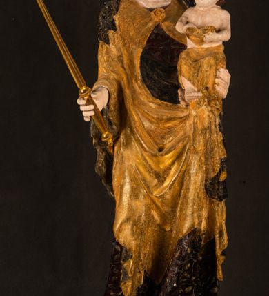 Zdjęcie nr 13: Rzeźba drążona ustawiona na niewielkim, wielobocznym postumencie. Maria ukazana w pozycji stojącej, frontalnie z ciałem ułożonym z lekkim kontrapoście. Lewą ręką podtrzymuje Dzieciątko Jezus, w prawej trzyma złocone berło zwieńczone kwiatem. Matka Boska przedstawiona jako młoda kobieta o podłużnej twarzy z wysokim czołem, migdałowatymi oczami oraz krótkim nosem i małymi ustami ułożonymi w delikatny uśmiech. Karnacja jasna, policzki wyraźnie zaróżowione. Długie, ciemne i falowane włosy rozdzielone przedziałkiem opadają na ramiona postaci. Na głowie Marii ciemna chusta oraz złocona korona (pozostałość korony?) lub diadem. Madonna jest ubrana w ciemną suknię z długimi rękawami dekorowaną motywem roślinnym oraz złocony płaszcz spięty pod szyją klamrą w kształcie kwiatu. Dzieciątko Jezus przedstawione w pozycji siedzącej z głową mocno pochyloną w bok i skrzyżowanymi stópkami. W ręku trzyma otwartą księgę. Twarz owalna, pulchna, ciemne oczy skierowane w lewo, usta w wyraźnym uśmiechu. Włosy, krótkie, falowane w kolorze brązowym. Dzieciątko jest ubrane w złoconą tkaninę udrapowaną wokół bioder. Figura polichromowana i częściowo złocona. Na odwrociu napis „Powtóre odzłocona / zarządem x(iędza) / Pawła Pomian Izdeb / skiego przez / Karol(a) Rośka / R(oku) P(ańskiego) 1853”.