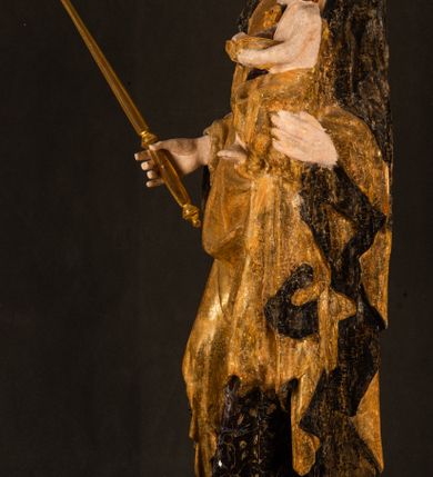 Zdjęcie nr 21: Rzeźba drążona ustawiona na niewielkim, wielobocznym postumencie. Maria ukazana w pozycji stojącej, frontalnie z ciałem ułożonym z lekkim kontrapoście. Lewą ręką podtrzymuje Dzieciątko Jezus, w prawej trzyma złocone berło zwieńczone kwiatem. Matka Boska przedstawiona jako młoda kobieta o podłużnej twarzy z wysokim czołem, migdałowatymi oczami oraz krótkim nosem i małymi ustami ułożonymi w delikatny uśmiech. Karnacja jasna, policzki wyraźnie zaróżowione. Długie, ciemne i falowane włosy rozdzielone przedziałkiem opadają na ramiona postaci. Na głowie Marii ciemna chusta oraz złocona korona (pozostałość korony?) lub diadem. Madonna jest ubrana w ciemną suknię z długimi rękawami dekorowaną motywem roślinnym oraz złocony płaszcz spięty pod szyją klamrą w kształcie kwiatu. Dzieciątko Jezus przedstawione w pozycji siedzącej z głową mocno pochyloną w bok i skrzyżowanymi stópkami. W ręku trzyma otwartą księgę. Twarz owalna, pulchna, ciemne oczy skierowane w lewo, usta w wyraźnym uśmiechu. Włosy, krótkie, falowane w kolorze brązowym. Dzieciątko jest ubrane w złoconą tkaninę udrapowaną wokół bioder. Figura polichromowana i częściowo złocona. Na odwrociu napis „Powtóre odzłocona / zarządem x(iędza) / Pawła Pomian Izdeb / skiego przez / Karol(a) Rośka / R(oku) P(ańskiego) 1853”.