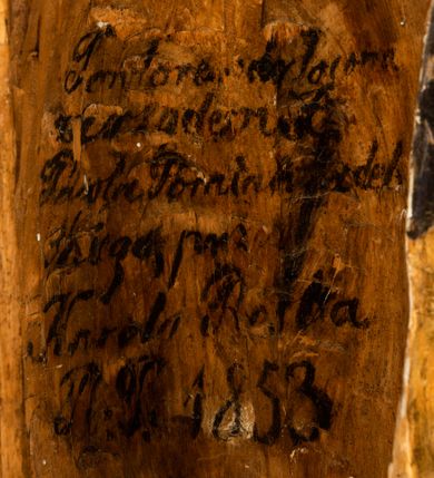 Zdjęcie nr 3: Rzeźba drążona ustawiona na niewielkim, wielobocznym postumencie. Maria ukazana w pozycji stojącej, frontalnie z ciałem ułożonym z lekkim kontrapoście. Lewą ręką podtrzymuje Dzieciątko Jezus, w prawej trzyma złocone berło zwieńczone kwiatem. Matka Boska przedstawiona jako młoda kobieta o podłużnej twarzy z wysokim czołem, migdałowatymi oczami oraz krótkim nosem i małymi ustami ułożonymi w delikatny uśmiech. Karnacja jasna, policzki wyraźnie zaróżowione. Długie, ciemne i falowane włosy rozdzielone przedziałkiem opadają na ramiona postaci. Na głowie Marii ciemna chusta oraz złocona korona (pozostałość korony?) lub diadem. Madonna jest ubrana w ciemną suknię z długimi rękawami dekorowaną motywem roślinnym oraz złocony płaszcz spięty pod szyją klamrą w kształcie kwiatu. Dzieciątko Jezus przedstawione w pozycji siedzącej z głową mocno pochyloną w bok i skrzyżowanymi stópkami. W ręku trzyma otwartą księgę. Twarz owalna, pulchna, ciemne oczy skierowane w lewo, usta w wyraźnym uśmiechu. Włosy, krótkie, falowane w kolorze brązowym. Dzieciątko jest ubrane w złoconą tkaninę udrapowaną wokół bioder. Figura polichromowana i częściowo złocona. Na odwrociu napis „Powtóre odzłocona / zarządem x(iędza) / Pawła Pomian Izdeb / skiego przez / Karol(a) Rośka / R(oku) P(ańskiego) 1853”.