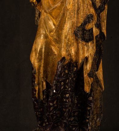 Zdjęcie nr 4: Rzeźba drążona ustawiona na niewielkim, wielobocznym postumencie. Maria ukazana w pozycji stojącej, frontalnie z ciałem ułożonym z lekkim kontrapoście. Lewą ręką podtrzymuje Dzieciątko Jezus, w prawej trzyma złocone berło zwieńczone kwiatem. Matka Boska przedstawiona jako młoda kobieta o podłużnej twarzy z wysokim czołem, migdałowatymi oczami oraz krótkim nosem i małymi ustami ułożonymi w delikatny uśmiech. Karnacja jasna, policzki wyraźnie zaróżowione. Długie, ciemne i falowane włosy rozdzielone przedziałkiem opadają na ramiona postaci. Na głowie Marii ciemna chusta oraz złocona korona (pozostałość korony?) lub diadem. Madonna jest ubrana w ciemną suknię z długimi rękawami dekorowaną motywem roślinnym oraz złocony płaszcz spięty pod szyją klamrą w kształcie kwiatu. Dzieciątko Jezus przedstawione w pozycji siedzącej z głową mocno pochyloną w bok i skrzyżowanymi stópkami. W ręku trzyma otwartą księgę. Twarz owalna, pulchna, ciemne oczy skierowane w lewo, usta w wyraźnym uśmiechu. Włosy, krótkie, falowane w kolorze brązowym. Dzieciątko jest ubrane w złoconą tkaninę udrapowaną wokół bioder. Figura polichromowana i częściowo złocona. Na odwrociu napis „Powtóre odzłocona / zarządem x(iędza) / Pawła Pomian Izdeb / skiego przez / Karol(a) Rośka / R(oku) P(ańskiego) 1853”.