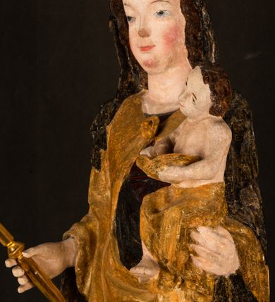 Zdjęcie nr 10: Rzeźba drążona ustawiona na niewielkim, wielobocznym postumencie. Maria ukazana w pozycji stojącej, frontalnie z ciałem ułożonym z lekkim kontrapoście. Lewą ręką podtrzymuje Dzieciątko Jezus, w prawej trzyma złocone berło zwieńczone kwiatem. Matka Boska przedstawiona jako młoda kobieta o podłużnej twarzy z wysokim czołem, migdałowatymi oczami oraz krótkim nosem i małymi ustami ułożonymi w delikatny uśmiech. Karnacja jasna, policzki wyraźnie zaróżowione. Długie, ciemne i falowane włosy rozdzielone przedziałkiem opadają na ramiona postaci. Na głowie Marii ciemna chusta oraz złocona korona (pozostałość korony?) lub diadem. Madonna jest ubrana w ciemną suknię z długimi rękawami dekorowaną motywem roślinnym oraz złocony płaszcz spięty pod szyją klamrą w kształcie kwiatu. Dzieciątko Jezus przedstawione w pozycji siedzącej z głową mocno pochyloną w bok i skrzyżowanymi stópkami. W ręku trzyma otwartą księgę. Twarz owalna, pulchna, ciemne oczy skierowane w lewo, usta w wyraźnym uśmiechu. Włosy, krótkie, falowane w kolorze brązowym. Dzieciątko jest ubrane w złoconą tkaninę udrapowaną wokół bioder. Figura polichromowana i częściowo złocona. Na odwrociu napis „Powtóre odzłocona / zarządem x(iędza) / Pawła Pomian Izdeb / skiego przez / Karol(a) Rośka / R(oku) P(ańskiego) 1853”.