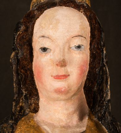 Zdjęcie nr 15: Rzeźba drążona ustawiona na niewielkim, wielobocznym postumencie. Maria ukazana w pozycji stojącej, frontalnie z ciałem ułożonym z lekkim kontrapoście. Lewą ręką podtrzymuje Dzieciątko Jezus, w prawej trzyma złocone berło zwieńczone kwiatem. Matka Boska przedstawiona jako młoda kobieta o podłużnej twarzy z wysokim czołem, migdałowatymi oczami oraz krótkim nosem i małymi ustami ułożonymi w delikatny uśmiech. Karnacja jasna, policzki wyraźnie zaróżowione. Długie, ciemne i falowane włosy rozdzielone przedziałkiem opadają na ramiona postaci. Na głowie Marii ciemna chusta oraz złocona korona (pozostałość korony?) lub diadem. Madonna jest ubrana w ciemną suknię z długimi rękawami dekorowaną motywem roślinnym oraz złocony płaszcz spięty pod szyją klamrą w kształcie kwiatu. Dzieciątko Jezus przedstawione w pozycji siedzącej z głową mocno pochyloną w bok i skrzyżowanymi stópkami. W ręku trzyma otwartą księgę. Twarz owalna, pulchna, ciemne oczy skierowane w lewo, usta w wyraźnym uśmiechu. Włosy, krótkie, falowane w kolorze brązowym. Dzieciątko jest ubrane w złoconą tkaninę udrapowaną wokół bioder. Figura polichromowana i częściowo złocona. Na odwrociu napis „Powtóre odzłocona / zarządem x(iędza) / Pawła Pomian Izdeb / skiego przez / Karol(a) Rośka / R(oku) P(ańskiego) 1853”.