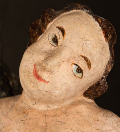 Zdjęcie nr 20: Rzeźba drążona ustawiona na niewielkim, wielobocznym postumencie. Maria ukazana w pozycji stojącej, frontalnie z ciałem ułożonym z lekkim kontrapoście. Lewą ręką podtrzymuje Dzieciątko Jezus, w prawej trzyma złocone berło zwieńczone kwiatem. Matka Boska przedstawiona jako młoda kobieta o podłużnej twarzy z wysokim czołem, migdałowatymi oczami oraz krótkim nosem i małymi ustami ułożonymi w delikatny uśmiech. Karnacja jasna, policzki wyraźnie zaróżowione. Długie, ciemne i falowane włosy rozdzielone przedziałkiem opadają na ramiona postaci. Na głowie Marii ciemna chusta oraz złocona korona (pozostałość korony?) lub diadem. Madonna jest ubrana w ciemną suknię z długimi rękawami dekorowaną motywem roślinnym oraz złocony płaszcz spięty pod szyją klamrą w kształcie kwiatu. Dzieciątko Jezus przedstawione w pozycji siedzącej z głową mocno pochyloną w bok i skrzyżowanymi stópkami. W ręku trzyma otwartą księgę. Twarz owalna, pulchna, ciemne oczy skierowane w lewo, usta w wyraźnym uśmiechu. Włosy, krótkie, falowane w kolorze brązowym. Dzieciątko jest ubrane w złoconą tkaninę udrapowaną wokół bioder. Figura polichromowana i częściowo złocona. Na odwrociu napis „Powtóre odzłocona / zarządem x(iędza) / Pawła Pomian Izdeb / skiego przez / Karol(a) Rośka / R(oku) P(ańskiego) 1853”.