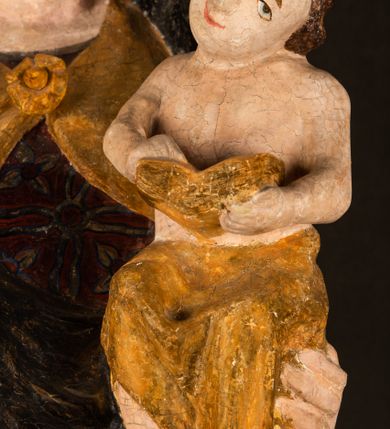 Zdjęcie nr 19: Rzeźba drążona ustawiona na niewielkim, wielobocznym postumencie. Maria ukazana w pozycji stojącej, frontalnie z ciałem ułożonym z lekkim kontrapoście. Lewą ręką podtrzymuje Dzieciątko Jezus, w prawej trzyma złocone berło zwieńczone kwiatem. Matka Boska przedstawiona jako młoda kobieta o podłużnej twarzy z wysokim czołem, migdałowatymi oczami oraz krótkim nosem i małymi ustami ułożonymi w delikatny uśmiech. Karnacja jasna, policzki wyraźnie zaróżowione. Długie, ciemne i falowane włosy rozdzielone przedziałkiem opadają na ramiona postaci. Na głowie Marii ciemna chusta oraz złocona korona (pozostałość korony?) lub diadem. Madonna jest ubrana w ciemną suknię z długimi rękawami dekorowaną motywem roślinnym oraz złocony płaszcz spięty pod szyją klamrą w kształcie kwiatu. Dzieciątko Jezus przedstawione w pozycji siedzącej z głową mocno pochyloną w bok i skrzyżowanymi stópkami. W ręku trzyma otwartą księgę. Twarz owalna, pulchna, ciemne oczy skierowane w lewo, usta w wyraźnym uśmiechu. Włosy, krótkie, falowane w kolorze brązowym. Dzieciątko jest ubrane w złoconą tkaninę udrapowaną wokół bioder. Figura polichromowana i częściowo złocona. Na odwrociu napis „Powtóre odzłocona / zarządem x(iędza) / Pawła Pomian Izdeb / skiego przez / Karol(a) Rośka / R(oku) P(ańskiego) 1853”.