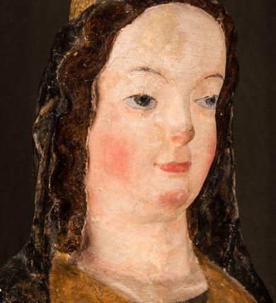 Zdjęcie nr 16: Rzeźba drążona ustawiona na niewielkim, wielobocznym postumencie. Maria ukazana w pozycji stojącej, frontalnie z ciałem ułożonym z lekkim kontrapoście. Lewą ręką podtrzymuje Dzieciątko Jezus, w prawej trzyma złocone berło zwieńczone kwiatem. Matka Boska przedstawiona jako młoda kobieta o podłużnej twarzy z wysokim czołem, migdałowatymi oczami oraz krótkim nosem i małymi ustami ułożonymi w delikatny uśmiech. Karnacja jasna, policzki wyraźnie zaróżowione. Długie, ciemne i falowane włosy rozdzielone przedziałkiem opadają na ramiona postaci. Na głowie Marii ciemna chusta oraz złocona korona (pozostałość korony?) lub diadem. Madonna jest ubrana w ciemną suknię z długimi rękawami dekorowaną motywem roślinnym oraz złocony płaszcz spięty pod szyją klamrą w kształcie kwiatu. Dzieciątko Jezus przedstawione w pozycji siedzącej z głową mocno pochyloną w bok i skrzyżowanymi stópkami. W ręku trzyma otwartą księgę. Twarz owalna, pulchna, ciemne oczy skierowane w lewo, usta w wyraźnym uśmiechu. Włosy, krótkie, falowane w kolorze brązowym. Dzieciątko jest ubrane w złoconą tkaninę udrapowaną wokół bioder. Figura polichromowana i częściowo złocona. Na odwrociu napis „Powtóre odzłocona / zarządem x(iędza) / Pawła Pomian Izdeb / skiego przez / Karol(a) Rośka / R(oku) P(ańskiego) 1853”.