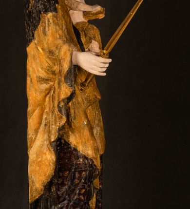 Zdjęcie nr 24: Rzeźba drążona ustawiona na niewielkim, wielobocznym postumencie. Maria ukazana w pozycji stojącej, frontalnie z ciałem ułożonym z lekkim kontrapoście. Lewą ręką podtrzymuje Dzieciątko Jezus, w prawej trzyma złocone berło zwieńczone kwiatem. Matka Boska przedstawiona jako młoda kobieta o podłużnej twarzy z wysokim czołem, migdałowatymi oczami oraz krótkim nosem i małymi ustami ułożonymi w delikatny uśmiech. Karnacja jasna, policzki wyraźnie zaróżowione. Długie, ciemne i falowane włosy rozdzielone przedziałkiem opadają na ramiona postaci. Na głowie Marii ciemna chusta oraz złocona korona (pozostałość korony?) lub diadem. Madonna jest ubrana w ciemną suknię z długimi rękawami dekorowaną motywem roślinnym oraz złocony płaszcz spięty pod szyją klamrą w kształcie kwiatu. Dzieciątko Jezus przedstawione w pozycji siedzącej z głową mocno pochyloną w bok i skrzyżowanymi stópkami. W ręku trzyma otwartą księgę. Twarz owalna, pulchna, ciemne oczy skierowane w lewo, usta w wyraźnym uśmiechu. Włosy, krótkie, falowane w kolorze brązowym. Dzieciątko jest ubrane w złoconą tkaninę udrapowaną wokół bioder. Figura polichromowana i częściowo złocona. Na odwrociu napis „Powtóre odzłocona / zarządem x(iędza) / Pawła Pomian Izdeb / skiego przez / Karol(a) Rośka / R(oku) P(ańskiego) 1853”.