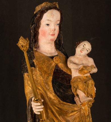 Zdjęcie nr 1: Rzeźba drążona ustawiona na niewielkim, wielobocznym postumencie. Maria ukazana w pozycji stojącej, frontalnie z ciałem ułożonym z lekkim kontrapoście. Lewą ręką podtrzymuje Dzieciątko Jezus, w prawej trzyma złocone berło zwieńczone kwiatem. Matka Boska przedstawiona jako młoda kobieta o podłużnej twarzy z wysokim czołem, migdałowatymi oczami oraz krótkim nosem i małymi ustami ułożonymi w delikatny uśmiech. Karnacja jasna, policzki wyraźnie zaróżowione. Długie, ciemne i falowane włosy rozdzielone przedziałkiem opadają na ramiona postaci. Na głowie Marii ciemna chusta oraz złocona korona (pozostałość korony?) lub diadem. Madonna jest ubrana w ciemną suknię z długimi rękawami dekorowaną motywem roślinnym oraz złocony płaszcz spięty pod szyją klamrą w kształcie kwiatu. Dzieciątko Jezus przedstawione w pozycji siedzącej z głową mocno pochyloną w bok i skrzyżowanymi stópkami. W ręku trzyma otwartą księgę. Twarz owalna, pulchna, ciemne oczy skierowane w lewo, usta w wyraźnym uśmiechu. Włosy, krótkie, falowane w kolorze brązowym. Dzieciątko jest ubrane w złoconą tkaninę udrapowaną wokół bioder. Figura polichromowana i częściowo złocona. Na odwrociu napis „Powtóre odzłocona / zarządem x(iędza) / Pawła Pomian Izdeb / skiego przez / Karol(a) Rośka / R(oku) P(ańskiego) 1853”.
