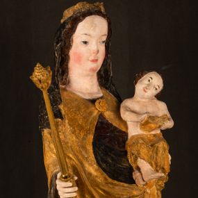 Zdjęcie nr 1: Rzeźba drążona ustawiona na niewielkim, wielobocznym postumencie. Maria ukazana w pozycji stojącej, frontalnie z ciałem ułożonym z lekkim kontrapoście. Lewą ręką podtrzymuje Dzieciątko Jezus, w prawej trzyma złocone berło zwieńczone kwiatem. Matka Boska przedstawiona jako młoda kobieta o podłużnej twarzy z wysokim czołem, migdałowatymi oczami oraz krótkim nosem i małymi ustami ułożonymi w delikatny uśmiech. Karnacja jasna, policzki wyraźnie zaróżowione. Długie, ciemne i falowane włosy rozdzielone przedziałkiem opadają na ramiona postaci. Na głowie Marii ciemna chusta oraz złocona korona (pozostałość korony?) lub diadem. Madonna jest ubrana w ciemną suknię z długimi rękawami dekorowaną motywem roślinnym oraz złocony płaszcz spięty pod szyją klamrą w kształcie kwiatu. Dzieciątko Jezus przedstawione w pozycji siedzącej z głową mocno pochyloną w bok i skrzyżowanymi stópkami. W ręku trzyma otwartą księgę. Twarz owalna, pulchna, ciemne oczy skierowane w lewo, usta w wyraźnym uśmiechu. Włosy, krótkie, falowane w kolorze brązowym. Dzieciątko jest ubrane w złoconą tkaninę udrapowaną wokół bioder. Figura polichromowana i częściowo złocona. Na odwrociu napis „Powtóre odzłocona / zarządem x(iędza) / Pawła Pomian Izdeb / skiego przez / Karol(a) Rośka / R(oku) P(ańskiego) 1853”.