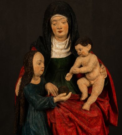 Zdjęcie nr 1: Rzeźba drążona przedstawiająca siedzącą św. Annę w towarzystwie klęczącej Marii oraz Dzieciątka Jezus. Anna ukazana frontalnie, z głową pochyloną nieznacznie w dół, obejmująca rękoma przedstawioną z prawej strony Marię oraz znajdujące się po lewej stronie Dzieciątko Jezus. Twarz świętej owalna o spokojnym wyrazie, z oczami skierowanymi w dół. Nos długi, prosty, na policzkach zaznaczony delikatny rumieniec. Anna ubrana jest w ciemnozieloną suknię przepasaną w talii, ciemnogranatową chustę zarzuconą na głowę, pod którą znajduje się biała podwika. Na ramiona i kolana postaci narzucony jest obszerny, czerwony płaszcz spod, którego widoczny jest ostro zakończony czubek brązowego buta św. Anny. Maria znajdująca się z lewej strony kompozycji została  przedstawiona jako młoda kobieta, klęcząca u stóp swojej matki i zwracająca się w kierunku siedzącego na kolanach Anny Dzieciątka Jezus. Owalną twarz Marii charakteryzuje wysokie czoło i cienkie, łukowato wygięte brwi. Długie, ciemne i lekko falowane włosy opadają na ramiona i plecy postaci. Maria swoją prawą rękę wspiera na kolanach Anny, lewą wyciąga przed siebie, podając Dzieciątku jabłko królewskie. Ubrana jest w ciemnogranatową suknię z długimi rękawami, spod której widoczne są bose stopy. Chrystus został ukazany jako nagi, ciemnowłosy chłopiec  o okrągłej twarzy z rumieńcem siedzący na kolanach św. Anny i wyciągający obie ręce w kierunku Marii. Rzeźba w pełni polichromowana.