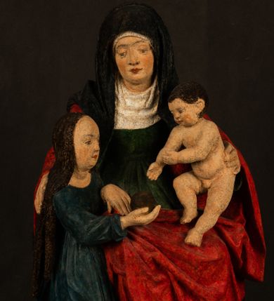 Zdjęcie nr 1: Rzeźba drążona przedstawiająca siedzącą św. Annę w towarzystwie klęczącej Marii oraz Dzieciątka Jezus. Anna ukazana frontalnie, z głową pochyloną nieznacznie w dół, obejmująca rękoma przedstawioną z prawej strony Marię oraz znajdujące się po lewej stronie Dzieciątko Jezus. Twarz świętej owalna o spokojnym wyrazie, z oczami skierowanymi w dół. Nos długi, prosty, na policzkach zaznaczony delikatny rumieniec. Anna ubrana jest w ciemnozieloną suknię przepasaną w talii, ciemnogranatową chustę zarzuconą na głowę, pod którą znajduje się biała podwika. Na ramiona i kolana postaci narzucony jest obszerny, czerwony płaszcz spod, którego widoczny jest ostro zakończony czubek brązowego buta św. Anny. Maria znajdująca się z lewej strony kompozycji została  przedstawiona jako młoda kobieta, klęcząca u stóp swojej matki i zwracająca się w kierunku siedzącego na kolanach Anny Dzieciątka Jezus. Owalną twarz Marii charakteryzuje wysokie czoło i cienkie, łukowato wygięte brwi. Długie, ciemne i lekko falowane włosy opadają na ramiona i plecy postaci. Maria swoją prawą rękę wspiera na kolanach Anny, lewą wyciąga przed siebie, podając Dzieciątku jabłko królewskie. Ubrana jest w ciemnogranatową suknię z długimi rękawami, spod której widoczne są bose stopy. Chrystus został ukazany jako nagi, ciemnowłosy chłopiec  o okrągłej twarzy z rumieńcem siedzący na kolanach św. Anny i wyciągający obie ręce w kierunku Marii. Rzeźba w pełni polichromowana.