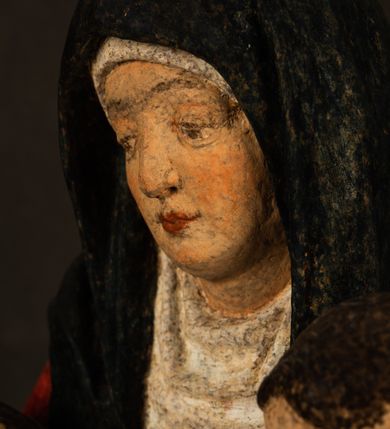 Zdjęcie nr 7: Rzeźba drążona przedstawiająca siedzącą św. Annę w towarzystwie klęczącej Marii oraz Dzieciątka Jezus. Anna ukazana frontalnie, z głową pochyloną nieznacznie w dół, obejmująca rękoma przedstawioną z prawej strony Marię oraz znajdujące się po lewej stronie Dzieciątko Jezus. Twarz świętej owalna o spokojnym wyrazie, z oczami skierowanymi w dół. Nos długi, prosty, na policzkach zaznaczony delikatny rumieniec. Anna ubrana jest w ciemnozieloną suknię przepasaną w talii, ciemnogranatową chustę zarzuconą na głowę, pod którą znajduje się biała podwika. Na ramiona i kolana postaci narzucony jest obszerny, czerwony płaszcz spod, którego widoczny jest ostro zakończony czubek brązowego buta św. Anny. Maria znajdująca się z lewej strony kompozycji została  przedstawiona jako młoda kobieta, klęcząca u stóp swojej matki i zwracająca się w kierunku siedzącego na kolanach Anny Dzieciątka Jezus. Owalną twarz Marii charakteryzuje wysokie czoło i cienkie, łukowato wygięte brwi. Długie, ciemne i lekko falowane włosy opadają na ramiona i plecy postaci. Maria swoją prawą rękę wspiera na kolanach Anny, lewą wyciąga przed siebie, podając Dzieciątku jabłko królewskie. Ubrana jest w ciemnogranatową suknię z długimi rękawami, spod której widoczne są bose stopy. Chrystus został ukazany jako nagi, ciemnowłosy chłopiec  o okrągłej twarzy z rumieńcem siedzący na kolanach św. Anny i wyciągający obie ręce w kierunku Marii. Rzeźba w pełni polichromowana.