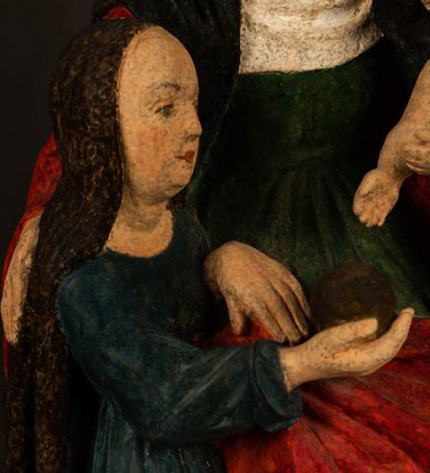 Zdjęcie nr 8: Rzeźba drążona przedstawiająca siedzącą św. Annę w towarzystwie klęczącej Marii oraz Dzieciątka Jezus. Anna ukazana frontalnie, z głową pochyloną nieznacznie w dół, obejmująca rękoma przedstawioną z prawej strony Marię oraz znajdujące się po lewej stronie Dzieciątko Jezus. Twarz świętej owalna o spokojnym wyrazie, z oczami skierowanymi w dół. Nos długi, prosty, na policzkach zaznaczony delikatny rumieniec. Anna ubrana jest w ciemnozieloną suknię przepasaną w talii, ciemnogranatową chustę zarzuconą na głowę, pod którą znajduje się biała podwika. Na ramiona i kolana postaci narzucony jest obszerny, czerwony płaszcz spod, którego widoczny jest ostro zakończony czubek brązowego buta św. Anny. Maria znajdująca się z lewej strony kompozycji została  przedstawiona jako młoda kobieta, klęcząca u stóp swojej matki i zwracająca się w kierunku siedzącego na kolanach Anny Dzieciątka Jezus. Owalną twarz Marii charakteryzuje wysokie czoło i cienkie, łukowato wygięte brwi. Długie, ciemne i lekko falowane włosy opadają na ramiona i plecy postaci. Maria swoją prawą rękę wspiera na kolanach Anny, lewą wyciąga przed siebie, podając Dzieciątku jabłko królewskie. Ubrana jest w ciemnogranatową suknię z długimi rękawami, spod której widoczne są bose stopy. Chrystus został ukazany jako nagi, ciemnowłosy chłopiec  o okrągłej twarzy z rumieńcem siedzący na kolanach św. Anny i wyciągający obie ręce w kierunku Marii. Rzeźba w pełni polichromowana.