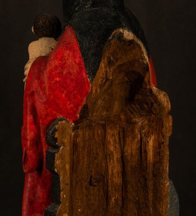 Zdjęcie nr 15: Rzeźba drążona przedstawiająca siedzącą św. Annę w towarzystwie klęczącej Marii oraz Dzieciątka Jezus. Anna ukazana frontalnie, z głową pochyloną nieznacznie w dół, obejmująca rękoma przedstawioną z prawej strony Marię oraz znajdujące się po lewej stronie Dzieciątko Jezus. Twarz świętej owalna o spokojnym wyrazie, z oczami skierowanymi w dół. Nos długi, prosty, na policzkach zaznaczony delikatny rumieniec. Anna ubrana jest w ciemnozieloną suknię przepasaną w talii, ciemnogranatową chustę zarzuconą na głowę, pod którą znajduje się biała podwika. Na ramiona i kolana postaci narzucony jest obszerny, czerwony płaszcz spod, którego widoczny jest ostro zakończony czubek brązowego buta św. Anny. Maria znajdująca się z lewej strony kompozycji została  przedstawiona jako młoda kobieta, klęcząca u stóp swojej matki i zwracająca się w kierunku siedzącego na kolanach Anny Dzieciątka Jezus. Owalną twarz Marii charakteryzuje wysokie czoło i cienkie, łukowato wygięte brwi. Długie, ciemne i lekko falowane włosy opadają na ramiona i plecy postaci. Maria swoją prawą rękę wspiera na kolanach Anny, lewą wyciąga przed siebie, podając Dzieciątku jabłko królewskie. Ubrana jest w ciemnogranatową suknię z długimi rękawami, spod której widoczne są bose stopy. Chrystus został ukazany jako nagi, ciemnowłosy chłopiec  o okrągłej twarzy z rumieńcem siedzący na kolanach św. Anny i wyciągający obie ręce w kierunku Marii. Rzeźba w pełni polichromowana.