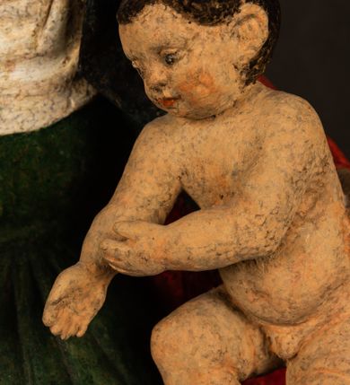 Zdjęcie nr 5: Rzeźba drążona przedstawiająca siedzącą św. Annę w towarzystwie klęczącej Marii oraz Dzieciątka Jezus. Anna ukazana frontalnie, z głową pochyloną nieznacznie w dół, obejmująca rękoma przedstawioną z prawej strony Marię oraz znajdujące się po lewej stronie Dzieciątko Jezus. Twarz świętej owalna o spokojnym wyrazie, z oczami skierowanymi w dół. Nos długi, prosty, na policzkach zaznaczony delikatny rumieniec. Anna ubrana jest w ciemnozieloną suknię przepasaną w talii, ciemnogranatową chustę zarzuconą na głowę, pod którą znajduje się biała podwika. Na ramiona i kolana postaci narzucony jest obszerny, czerwony płaszcz spod, którego widoczny jest ostro zakończony czubek brązowego buta św. Anny. Maria znajdująca się z lewej strony kompozycji została  przedstawiona jako młoda kobieta, klęcząca u stóp swojej matki i zwracająca się w kierunku siedzącego na kolanach Anny Dzieciątka Jezus. Owalną twarz Marii charakteryzuje wysokie czoło i cienkie, łukowato wygięte brwi. Długie, ciemne i lekko falowane włosy opadają na ramiona i plecy postaci. Maria swoją prawą rękę wspiera na kolanach Anny, lewą wyciąga przed siebie, podając Dzieciątku jabłko królewskie. Ubrana jest w ciemnogranatową suknię z długimi rękawami, spod której widoczne są bose stopy. Chrystus został ukazany jako nagi, ciemnowłosy chłopiec  o okrągłej twarzy z rumieńcem siedzący na kolanach św. Anny i wyciągający obie ręce w kierunku Marii. Rzeźba w pełni polichromowana.