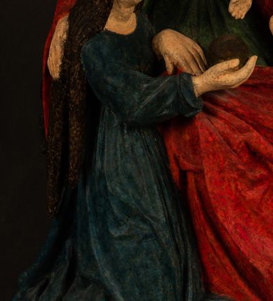 Zdjęcie nr 3: Rzeźba drążona przedstawiająca siedzącą św. Annę w towarzystwie klęczącej Marii oraz Dzieciątka Jezus. Anna ukazana frontalnie, z głową pochyloną nieznacznie w dół, obejmująca rękoma przedstawioną z prawej strony Marię oraz znajdujące się po lewej stronie Dzieciątko Jezus. Twarz świętej owalna o spokojnym wyrazie, z oczami skierowanymi w dół. Nos długi, prosty, na policzkach zaznaczony delikatny rumieniec. Anna ubrana jest w ciemnozieloną suknię przepasaną w talii, ciemnogranatową chustę zarzuconą na głowę, pod którą znajduje się biała podwika. Na ramiona i kolana postaci narzucony jest obszerny, czerwony płaszcz spod, którego widoczny jest ostro zakończony czubek brązowego buta św. Anny. Maria znajdująca się z lewej strony kompozycji została  przedstawiona jako młoda kobieta, klęcząca u stóp swojej matki i zwracająca się w kierunku siedzącego na kolanach Anny Dzieciątka Jezus. Owalną twarz Marii charakteryzuje wysokie czoło i cienkie, łukowato wygięte brwi. Długie, ciemne i lekko falowane włosy opadają na ramiona i plecy postaci. Maria swoją prawą rękę wspiera na kolanach Anny, lewą wyciąga przed siebie, podając Dzieciątku jabłko królewskie. Ubrana jest w ciemnogranatową suknię z długimi rękawami, spod której widoczne są bose stopy. Chrystus został ukazany jako nagi, ciemnowłosy chłopiec  o okrągłej twarzy z rumieńcem siedzący na kolanach św. Anny i wyciągający obie ręce w kierunku Marii. Rzeźba w pełni polichromowana.