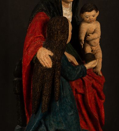 Zdjęcie nr 2: Rzeźba drążona przedstawiająca siedzącą św. Annę w towarzystwie klęczącej Marii oraz Dzieciątka Jezus. Anna ukazana frontalnie, z głową pochyloną nieznacznie w dół, obejmująca rękoma przedstawioną z prawej strony Marię oraz znajdujące się po lewej stronie Dzieciątko Jezus. Twarz świętej owalna o spokojnym wyrazie, z oczami skierowanymi w dół. Nos długi, prosty, na policzkach zaznaczony delikatny rumieniec. Anna ubrana jest w ciemnozieloną suknię przepasaną w talii, ciemnogranatową chustę zarzuconą na głowę, pod którą znajduje się biała podwika. Na ramiona i kolana postaci narzucony jest obszerny, czerwony płaszcz spod, którego widoczny jest ostro zakończony czubek brązowego buta św. Anny. Maria znajdująca się z lewej strony kompozycji została  przedstawiona jako młoda kobieta, klęcząca u stóp swojej matki i zwracająca się w kierunku siedzącego na kolanach Anny Dzieciątka Jezus. Owalną twarz Marii charakteryzuje wysokie czoło i cienkie, łukowato wygięte brwi. Długie, ciemne i lekko falowane włosy opadają na ramiona i plecy postaci. Maria swoją prawą rękę wspiera na kolanach Anny, lewą wyciąga przed siebie, podając Dzieciątku jabłko królewskie. Ubrana jest w ciemnogranatową suknię z długimi rękawami, spod której widoczne są bose stopy. Chrystus został ukazany jako nagi, ciemnowłosy chłopiec  o okrągłej twarzy z rumieńcem siedzący na kolanach św. Anny i wyciągający obie ręce w kierunku Marii. Rzeźba w pełni polichromowana.