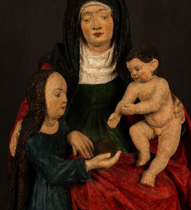 Zdjęcie nr 16: Rzeźba drążona przedstawiająca siedzącą św. Annę w towarzystwie klęczącej Marii oraz Dzieciątka Jezus. Anna ukazana frontalnie, z głową pochyloną nieznacznie w dół, obejmująca rękoma przedstawioną z prawej strony Marię oraz znajdujące się po lewej stronie Dzieciątko Jezus. Twarz świętej owalna o spokojnym wyrazie, z oczami skierowanymi w dół. Nos długi, prosty, na policzkach zaznaczony delikatny rumieniec. Anna ubrana jest w ciemnozieloną suknię przepasaną w talii, ciemnogranatową chustę zarzuconą na głowę, pod którą znajduje się biała podwika. Na ramiona i kolana postaci narzucony jest obszerny, czerwony płaszcz spod, którego widoczny jest ostro zakończony czubek brązowego buta św. Anny. Maria znajdująca się z lewej strony kompozycji została  przedstawiona jako młoda kobieta, klęcząca u stóp swojej matki i zwracająca się w kierunku siedzącego na kolanach Anny Dzieciątka Jezus. Owalną twarz Marii charakteryzuje wysokie czoło i cienkie, łukowato wygięte brwi. Długie, ciemne i lekko falowane włosy opadają na ramiona i plecy postaci. Maria swoją prawą rękę wspiera na kolanach Anny, lewą wyciąga przed siebie, podając Dzieciątku jabłko królewskie. Ubrana jest w ciemnogranatową suknię z długimi rękawami, spod której widoczne są bose stopy. Chrystus został ukazany jako nagi, ciemnowłosy chłopiec  o okrągłej twarzy z rumieńcem siedzący na kolanach św. Anny i wyciągający obie ręce w kierunku Marii. Rzeźba w pełni polichromowana.