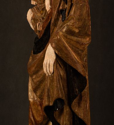 Zdjęcie nr 19: Przyścienna rzeźba Madonny z Dzieciątkiem jest z tyłu wydrążona. W tyle głowy Marii wbity jest hak służący do umocowania w ołtarzu. Matka Boska w całej postaci została ukazana w lekkim kontrapoście z charakterystycznym przegięciem w kształcie odwróconej litery &quot;S&quot;. Na prawej ręce trzyma Dzieciątko Jezus, lewą zaś ręką opuszczoną wzdłuż tułowia podtrzymuje nadgarstkiem fałdy płaszcza. Madonna ma pociągłą, zamyśloną twarz o jasnej karnacji, wysokie czoło i pucułowate, rumiane policzki. Ma prosty nos, migdałowe oczy oraz wydatne usta i podbródek. Jej głowę osadzoną na długiej szyi okalają zaczesane do tyłu brązowe włosy, widoczne spod osuwającej się chusty opadającej na ramiona dwoma festonami. Maria ubrana jest w złoconą suknię laserowaną ciepłą czerwienią oraz złocony płaszcz podbity srebrną podszewką z oliwkowo zielonym laserunkiem. Z przodu płaszcz drapowany jest w łukowate fałdy. Jedna z nich biegnie diagonalnie od prawej dłoni ku lewej stopie Madonny. Płaszcz po bokach postaci spływa rurkowatymi kaskadami. Maria na głowię ma wysoką, złotą koronę ze sterczynami o trójlistnych zakończeniach. Mały Jezus został ujęty w trzech czwartych z nieznacznie odchyloną głową do tyłu i skrzyżowanymi nóżkami. Lewą rękę kładzie na piersi matki, w prawej zaś trzyma złocone jabłko. Ma okrągłą, pucułowatą twarz o rumianych policzkach. Charakteryzuje ją prosty nosek, wydatne wargi i podbródek oraz wyraziste, szeroko otwarte oczy. Jego głowę z wysokim czołem okalają krótkie brązowe włosy. Ubrany jest w złocistą długą tunikę odsłaniającą fragmenty stóp.   