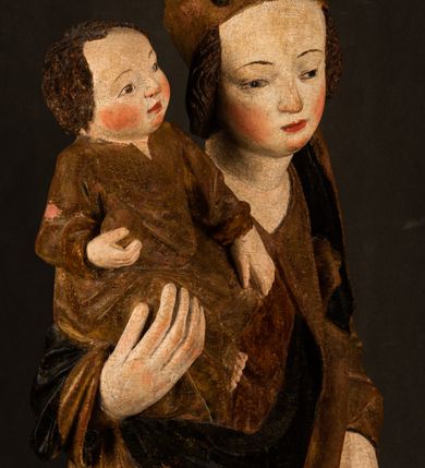 Zdjęcie nr 6: Przyścienna rzeźba Madonny z Dzieciątkiem jest z tyłu wydrążona. W tyle głowy Marii wbity jest hak służący do umocowania w ołtarzu. Matka Boska w całej postaci została ukazana w lekkim kontrapoście z charakterystycznym przegięciem w kształcie odwróconej litery "S". Na prawej ręce trzyma Dzieciątko Jezus, lewą zaś ręką opuszczoną wzdłuż tułowia podtrzymuje nadgarstkiem fałdy płaszcza. Madonna ma pociągłą, zamyśloną twarz o jasnej karnacji, wysokie czoło i pucułowate, rumiane policzki. Ma prosty nos, migdałowe oczy oraz wydatne usta i podbródek. Jej głowę osadzoną na długiej szyi okalają zaczesane do tyłu brązowe włosy, widoczne spod osuwającej się chusty opadającej na ramiona dwoma festonami. Maria ubrana jest w złoconą suknię laserowaną ciepłą czerwienią oraz złocony płaszcz podbity srebrną podszewką z oliwkowo zielonym laserunkiem. Z przodu płaszcz drapowany jest w łukowate fałdy. Jedna z nich biegnie diagonalnie od prawej dłoni ku lewej stopie Madonny. Płaszcz po bokach postaci spływa rurkowatymi kaskadami. Maria na głowię ma wysoką, złotą koronę ze sterczynami o trójlistnych zakończeniach. Mały Jezus został ujęty w trzech czwartych z nieznacznie odchyloną głową do tyłu i skrzyżowanymi nóżkami. Lewą rękę kładzie na piersi matki, w prawej zaś trzyma złocone jabłko. Ma okrągłą, pucułowatą twarz o rumianych policzkach. Charakteryzuje ją prosty nosek, wydatne wargi i podbródek oraz wyraziste, szeroko otwarte oczy. Jego głowę z wysokim czołem okalają krótkie brązowe włosy. Ubrany jest w złocistą długą tunikę odsłaniającą fragmenty stóp.   