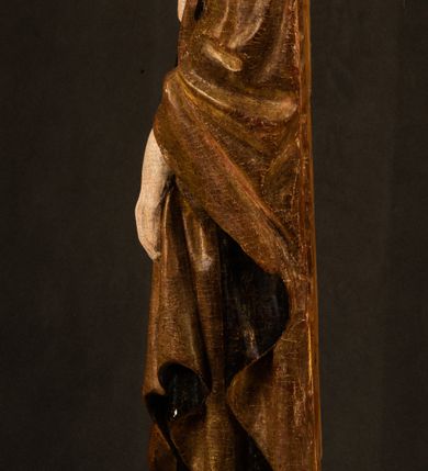 Zdjęcie nr 20: Przyścienna rzeźba Madonny z Dzieciątkiem jest z tyłu wydrążona. W tyle głowy Marii wbity jest hak służący do umocowania w ołtarzu. Matka Boska w całej postaci została ukazana w lekkim kontrapoście z charakterystycznym przegięciem w kształcie odwróconej litery &quot;S&quot;. Na prawej ręce trzyma Dzieciątko Jezus, lewą zaś ręką opuszczoną wzdłuż tułowia podtrzymuje nadgarstkiem fałdy płaszcza. Madonna ma pociągłą, zamyśloną twarz o jasnej karnacji, wysokie czoło i pucułowate, rumiane policzki. Ma prosty nos, migdałowe oczy oraz wydatne usta i podbródek. Jej głowę osadzoną na długiej szyi okalają zaczesane do tyłu brązowe włosy, widoczne spod osuwającej się chusty opadającej na ramiona dwoma festonami. Maria ubrana jest w złoconą suknię laserowaną ciepłą czerwienią oraz złocony płaszcz podbity srebrną podszewką z oliwkowo zielonym laserunkiem. Z przodu płaszcz drapowany jest w łukowate fałdy. Jedna z nich biegnie diagonalnie od prawej dłoni ku lewej stopie Madonny. Płaszcz po bokach postaci spływa rurkowatymi kaskadami. Maria na głowię ma wysoką, złotą koronę ze sterczynami o trójlistnych zakończeniach. Mały Jezus został ujęty w trzech czwartych z nieznacznie odchyloną głową do tyłu i skrzyżowanymi nóżkami. Lewą rękę kładzie na piersi matki, w prawej zaś trzyma złocone jabłko. Ma okrągłą, pucułowatą twarz o rumianych policzkach. Charakteryzuje ją prosty nosek, wydatne wargi i podbródek oraz wyraziste, szeroko otwarte oczy. Jego głowę z wysokim czołem okalają krótkie brązowe włosy. Ubrany jest w złocistą długą tunikę odsłaniającą fragmenty stóp.   