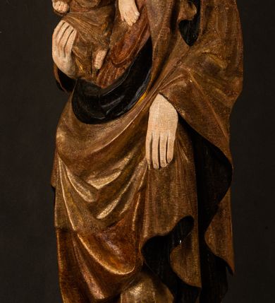 Zdjęcie nr 13: Przyścienna rzeźba Madonny z Dzieciątkiem jest z tyłu wydrążona. W tyle głowy Marii wbity jest hak służący do umocowania w ołtarzu. Matka Boska w całej postaci została ukazana w lekkim kontrapoście z charakterystycznym przegięciem w kształcie odwróconej litery &quot;S&quot;. Na prawej ręce trzyma Dzieciątko Jezus, lewą zaś ręką opuszczoną wzdłuż tułowia podtrzymuje nadgarstkiem fałdy płaszcza. Madonna ma pociągłą, zamyśloną twarz o jasnej karnacji, wysokie czoło i pucułowate, rumiane policzki. Ma prosty nos, migdałowe oczy oraz wydatne usta i podbródek. Jej głowę osadzoną na długiej szyi okalają zaczesane do tyłu brązowe włosy, widoczne spod osuwającej się chusty opadającej na ramiona dwoma festonami. Maria ubrana jest w złoconą suknię laserowaną ciepłą czerwienią oraz złocony płaszcz podbity srebrną podszewką z oliwkowo zielonym laserunkiem. Z przodu płaszcz drapowany jest w łukowate fałdy. Jedna z nich biegnie diagonalnie od prawej dłoni ku lewej stopie Madonny. Płaszcz po bokach postaci spływa rurkowatymi kaskadami. Maria na głowię ma wysoką, złotą koronę ze sterczynami o trójlistnych zakończeniach. Mały Jezus został ujęty w trzech czwartych z nieznacznie odchyloną głową do tyłu i skrzyżowanymi nóżkami. Lewą rękę kładzie na piersi matki, w prawej zaś trzyma złocone jabłko. Ma okrągłą, pucułowatą twarz o rumianych policzkach. Charakteryzuje ją prosty nosek, wydatne wargi i podbródek oraz wyraziste, szeroko otwarte oczy. Jego głowę z wysokim czołem okalają krótkie brązowe włosy. Ubrany jest w złocistą długą tunikę odsłaniającą fragmenty stóp.   