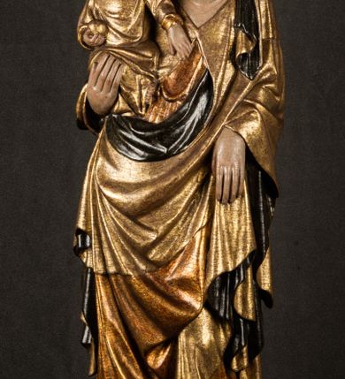 Zdjęcie nr 18: Przyścienna rzeźba Madonny z Dzieciątkiem jest z tyłu wydrążona. W tyle głowy Marii wbity jest hak służący do umocowania w ołtarzu. Matka Boska w całej postaci została ukazana w lekkim kontrapoście z charakterystycznym przegięciem w kształcie odwróconej litery &quot;S&quot;. Na prawej ręce trzyma Dzieciątko Jezus, lewą zaś ręką opuszczoną wzdłuż tułowia podtrzymuje nadgarstkiem fałdy płaszcza. Madonna ma pociągłą, zamyśloną twarz o jasnej karnacji, wysokie czoło i pucułowate, rumiane policzki. Ma prosty nos, migdałowe oczy oraz wydatne usta i podbródek. Jej głowę osadzoną na długiej szyi okalają zaczesane do tyłu brązowe włosy, widoczne spod osuwającej się chusty opadającej na ramiona dwoma festonami. Maria ubrana jest w złoconą suknię laserowaną ciepłą czerwienią oraz złocony płaszcz podbity srebrną podszewką z oliwkowo zielonym laserunkiem. Z przodu płaszcz drapowany jest w łukowate fałdy. Jedna z nich biegnie diagonalnie od prawej dłoni ku lewej stopie Madonny. Płaszcz po bokach postaci spływa rurkowatymi kaskadami. Maria na głowię ma wysoką, złotą koronę ze sterczynami o trójlistnych zakończeniach. Mały Jezus został ujęty w trzech czwartych z nieznacznie odchyloną głową do tyłu i skrzyżowanymi nóżkami. Lewą rękę kładzie na piersi matki, w prawej zaś trzyma złocone jabłko. Ma okrągłą, pucułowatą twarz o rumianych policzkach. Charakteryzuje ją prosty nosek, wydatne wargi i podbródek oraz wyraziste, szeroko otwarte oczy. Jego głowę z wysokim czołem okalają krótkie brązowe włosy. Ubrany jest w złocistą długą tunikę odsłaniającą fragmenty stóp.   