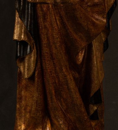 Zdjęcie nr 4: Przyścienna rzeźba Madonny z Dzieciątkiem jest z tyłu wydrążona. W tyle głowy Marii wbity jest hak służący do umocowania w ołtarzu. Matka Boska w całej postaci została ukazana w lekkim kontrapoście z charakterystycznym przegięciem w kształcie odwróconej litery "S". Na prawej ręce trzyma Dzieciątko Jezus, lewą zaś ręką opuszczoną wzdłuż tułowia podtrzymuje nadgarstkiem fałdy płaszcza. Madonna ma pociągłą, zamyśloną twarz o jasnej karnacji, wysokie czoło i pucułowate, rumiane policzki. Ma prosty nos, migdałowe oczy oraz wydatne usta i podbródek. Jej głowę osadzoną na długiej szyi okalają zaczesane do tyłu brązowe włosy, widoczne spod osuwającej się chusty opadającej na ramiona dwoma festonami. Maria ubrana jest w złoconą suknię laserowaną ciepłą czerwienią oraz złocony płaszcz podbity srebrną podszewką z oliwkowo zielonym laserunkiem. Z przodu płaszcz drapowany jest w łukowate fałdy. Jedna z nich biegnie diagonalnie od prawej dłoni ku lewej stopie Madonny. Płaszcz po bokach postaci spływa rurkowatymi kaskadami. Maria na głowię ma wysoką, złotą koronę ze sterczynami o trójlistnych zakończeniach. Mały Jezus został ujęty w trzech czwartych z nieznacznie odchyloną głową do tyłu i skrzyżowanymi nóżkami. Lewą rękę kładzie na piersi matki, w prawej zaś trzyma złocone jabłko. Ma okrągłą, pucułowatą twarz o rumianych policzkach. Charakteryzuje ją prosty nosek, wydatne wargi i podbródek oraz wyraziste, szeroko otwarte oczy. Jego głowę z wysokim czołem okalają krótkie brązowe włosy. Ubrany jest w złocistą długą tunikę odsłaniającą fragmenty stóp.   