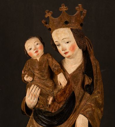 Zdjęcie nr 1: Przyścienna rzeźba Madonny z Dzieciątkiem jest z tyłu wydrążona. W tyle głowy Marii wbity jest hak służący do umocowania w ołtarzu. Matka Boska w całej postaci została ukazana w lekkim kontrapoście z charakterystycznym przegięciem w kształcie odwróconej litery &quot;S&quot;. Na prawej ręce trzyma Dzieciątko Jezus, lewą zaś ręką opuszczoną wzdłuż tułowia podtrzymuje nadgarstkiem fałdy płaszcza. Madonna ma pociągłą, zamyśloną twarz o jasnej karnacji, wysokie czoło i pucułowate, rumiane policzki. Ma prosty nos, migdałowe oczy oraz wydatne usta i podbródek. Jej głowę osadzoną na długiej szyi okalają zaczesane do tyłu brązowe włosy, widoczne spod osuwającej się chusty opadającej na ramiona dwoma festonami. Maria ubrana jest w złoconą suknię laserowaną ciepłą czerwienią oraz złocony płaszcz podbity srebrną podszewką z oliwkowo zielonym laserunkiem. Z przodu płaszcz drapowany jest w łukowate fałdy. Jedna z nich biegnie diagonalnie od prawej dłoni ku lewej stopie Madonny. Płaszcz po bokach postaci spływa rurkowatymi kaskadami. Maria na głowię ma wysoką, złotą koronę ze sterczynami o trójlistnych zakończeniach. Mały Jezus został ujęty w trzech czwartych z nieznacznie odchyloną głową do tyłu i skrzyżowanymi nóżkami. Lewą rękę kładzie na piersi matki, w prawej zaś trzyma złocone jabłko. Ma okrągłą, pucułowatą twarz o rumianych policzkach. Charakteryzuje ją prosty nosek, wydatne wargi i podbródek oraz wyraziste, szeroko otwarte oczy. Jego głowę z wysokim czołem okalają krótkie brązowe włosy. Ubrany jest w złocistą długą tunikę odsłaniającą fragmenty stóp.   