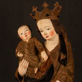 Zdjęcie nr 1: Przyścienna rzeźba Madonny z Dzieciątkiem jest z tyłu wydrążona. W tyle głowy Marii wbity jest hak służący do umocowania w ołtarzu. Matka Boska w całej postaci została ukazana w lekkim kontrapoście z charakterystycznym przegięciem w kształcie odwróconej litery &quot;S&quot;. Na prawej ręce trzyma Dzieciątko Jezus, lewą zaś ręką opuszczoną wzdłuż tułowia podtrzymuje nadgarstkiem fałdy płaszcza. Madonna ma pociągłą, zamyśloną twarz o jasnej karnacji, wysokie czoło i pucułowate, rumiane policzki. Ma prosty nos, migdałowe oczy oraz wydatne usta i podbródek. Jej głowę osadzoną na długiej szyi okalają zaczesane do tyłu brązowe włosy, widoczne spod osuwającej się chusty opadającej na ramiona dwoma festonami. Maria ubrana jest w złoconą suknię laserowaną ciepłą czerwienią oraz złocony płaszcz podbity srebrną podszewką z oliwkowo zielonym laserunkiem. Z przodu płaszcz drapowany jest w łukowate fałdy. Jedna z nich biegnie diagonalnie od prawej dłoni ku lewej stopie Madonny. Płaszcz po bokach postaci spływa rurkowatymi kaskadami. Maria na głowię ma wysoką, złotą koronę ze sterczynami o trójlistnych zakończeniach. Mały Jezus został ujęty w trzech czwartych z nieznacznie odchyloną głową do tyłu i skrzyżowanymi nóżkami. Lewą rękę kładzie na piersi matki, w prawej zaś trzyma złocone jabłko. Ma okrągłą, pucułowatą twarz o rumianych policzkach. Charakteryzuje ją prosty nosek, wydatne wargi i podbródek oraz wyraziste, szeroko otwarte oczy. Jego głowę z wysokim czołem okalają krótkie brązowe włosy. Ubrany jest w złocistą długą tunikę odsłaniającą fragmenty stóp.   