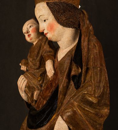 Zdjęcie nr 10: Przyścienna rzeźba Madonny z Dzieciątkiem jest z tyłu wydrążona. W tyle głowy Marii wbity jest hak służący do umocowania w ołtarzu. Matka Boska w całej postaci została ukazana w lekkim kontrapoście z charakterystycznym przegięciem w kształcie odwróconej litery "S". Na prawej ręce trzyma Dzieciątko Jezus, lewą zaś ręką opuszczoną wzdłuż tułowia podtrzymuje nadgarstkiem fałdy płaszcza. Madonna ma pociągłą, zamyśloną twarz o jasnej karnacji, wysokie czoło i pucułowate, rumiane policzki. Ma prosty nos, migdałowe oczy oraz wydatne usta i podbródek. Jej głowę osadzoną na długiej szyi okalają zaczesane do tyłu brązowe włosy, widoczne spod osuwającej się chusty opadającej na ramiona dwoma festonami. Maria ubrana jest w złoconą suknię laserowaną ciepłą czerwienią oraz złocony płaszcz podbity srebrną podszewką z oliwkowo zielonym laserunkiem. Z przodu płaszcz drapowany jest w łukowate fałdy. Jedna z nich biegnie diagonalnie od prawej dłoni ku lewej stopie Madonny. Płaszcz po bokach postaci spływa rurkowatymi kaskadami. Maria na głowię ma wysoką, złotą koronę ze sterczynami o trójlistnych zakończeniach. Mały Jezus został ujęty w trzech czwartych z nieznacznie odchyloną głową do tyłu i skrzyżowanymi nóżkami. Lewą rękę kładzie na piersi matki, w prawej zaś trzyma złocone jabłko. Ma okrągłą, pucułowatą twarz o rumianych policzkach. Charakteryzuje ją prosty nosek, wydatne wargi i podbródek oraz wyraziste, szeroko otwarte oczy. Jego głowę z wysokim czołem okalają krótkie brązowe włosy. Ubrany jest w złocistą długą tunikę odsłaniającą fragmenty stóp.   