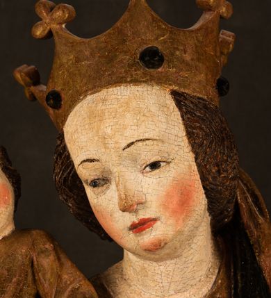 Zdjęcie nr 15: Przyścienna rzeźba Madonny z Dzieciątkiem jest z tyłu wydrążona. W tyle głowy Marii wbity jest hak służący do umocowania w ołtarzu. Matka Boska w całej postaci została ukazana w lekkim kontrapoście z charakterystycznym przegięciem w kształcie odwróconej litery "S". Na prawej ręce trzyma Dzieciątko Jezus, lewą zaś ręką opuszczoną wzdłuż tułowia podtrzymuje nadgarstkiem fałdy płaszcza. Madonna ma pociągłą, zamyśloną twarz o jasnej karnacji, wysokie czoło i pucułowate, rumiane policzki. Ma prosty nos, migdałowe oczy oraz wydatne usta i podbródek. Jej głowę osadzoną na długiej szyi okalają zaczesane do tyłu brązowe włosy, widoczne spod osuwającej się chusty opadającej na ramiona dwoma festonami. Maria ubrana jest w złoconą suknię laserowaną ciepłą czerwienią oraz złocony płaszcz podbity srebrną podszewką z oliwkowo zielonym laserunkiem. Z przodu płaszcz drapowany jest w łukowate fałdy. Jedna z nich biegnie diagonalnie od prawej dłoni ku lewej stopie Madonny. Płaszcz po bokach postaci spływa rurkowatymi kaskadami. Maria na głowię ma wysoką, złotą koronę ze sterczynami o trójlistnych zakończeniach. Mały Jezus został ujęty w trzech czwartych z nieznacznie odchyloną głową do tyłu i skrzyżowanymi nóżkami. Lewą rękę kładzie na piersi matki, w prawej zaś trzyma złocone jabłko. Ma okrągłą, pucułowatą twarz o rumianych policzkach. Charakteryzuje ją prosty nosek, wydatne wargi i podbródek oraz wyraziste, szeroko otwarte oczy. Jego głowę z wysokim czołem okalają krótkie brązowe włosy. Ubrany jest w złocistą długą tunikę odsłaniającą fragmenty stóp.   