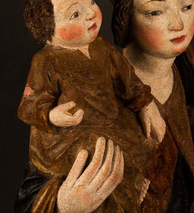 Zdjęcie nr 8: Przyścienna rzeźba Madonny z Dzieciątkiem jest z tyłu wydrążona. W tyle głowy Marii wbity jest hak służący do umocowania w ołtarzu. Matka Boska w całej postaci została ukazana w lekkim kontrapoście z charakterystycznym przegięciem w kształcie odwróconej litery &quot;S&quot;. Na prawej ręce trzyma Dzieciątko Jezus, lewą zaś ręką opuszczoną wzdłuż tułowia podtrzymuje nadgarstkiem fałdy płaszcza. Madonna ma pociągłą, zamyśloną twarz o jasnej karnacji, wysokie czoło i pucułowate, rumiane policzki. Ma prosty nos, migdałowe oczy oraz wydatne usta i podbródek. Jej głowę osadzoną na długiej szyi okalają zaczesane do tyłu brązowe włosy, widoczne spod osuwającej się chusty opadającej na ramiona dwoma festonami. Maria ubrana jest w złoconą suknię laserowaną ciepłą czerwienią oraz złocony płaszcz podbity srebrną podszewką z oliwkowo zielonym laserunkiem. Z przodu płaszcz drapowany jest w łukowate fałdy. Jedna z nich biegnie diagonalnie od prawej dłoni ku lewej stopie Madonny. Płaszcz po bokach postaci spływa rurkowatymi kaskadami. Maria na głowię ma wysoką, złotą koronę ze sterczynami o trójlistnych zakończeniach. Mały Jezus został ujęty w trzech czwartych z nieznacznie odchyloną głową do tyłu i skrzyżowanymi nóżkami. Lewą rękę kładzie na piersi matki, w prawej zaś trzyma złocone jabłko. Ma okrągłą, pucułowatą twarz o rumianych policzkach. Charakteryzuje ją prosty nosek, wydatne wargi i podbródek oraz wyraziste, szeroko otwarte oczy. Jego głowę z wysokim czołem okalają krótkie brązowe włosy. Ubrany jest w złocistą długą tunikę odsłaniającą fragmenty stóp.   