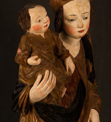 Zdjęcie nr 7: Przyścienna rzeźba Madonny z Dzieciątkiem jest z tyłu wydrążona. W tyle głowy Marii wbity jest hak służący do umocowania w ołtarzu. Matka Boska w całej postaci została ukazana w lekkim kontrapoście z charakterystycznym przegięciem w kształcie odwróconej litery &quot;S&quot;. Na prawej ręce trzyma Dzieciątko Jezus, lewą zaś ręką opuszczoną wzdłuż tułowia podtrzymuje nadgarstkiem fałdy płaszcza. Madonna ma pociągłą, zamyśloną twarz o jasnej karnacji, wysokie czoło i pucułowate, rumiane policzki. Ma prosty nos, migdałowe oczy oraz wydatne usta i podbródek. Jej głowę osadzoną na długiej szyi okalają zaczesane do tyłu brązowe włosy, widoczne spod osuwającej się chusty opadającej na ramiona dwoma festonami. Maria ubrana jest w złoconą suknię laserowaną ciepłą czerwienią oraz złocony płaszcz podbity srebrną podszewką z oliwkowo zielonym laserunkiem. Z przodu płaszcz drapowany jest w łukowate fałdy. Jedna z nich biegnie diagonalnie od prawej dłoni ku lewej stopie Madonny. Płaszcz po bokach postaci spływa rurkowatymi kaskadami. Maria na głowię ma wysoką, złotą koronę ze sterczynami o trójlistnych zakończeniach. Mały Jezus został ujęty w trzech czwartych z nieznacznie odchyloną głową do tyłu i skrzyżowanymi nóżkami. Lewą rękę kładzie na piersi matki, w prawej zaś trzyma złocone jabłko. Ma okrągłą, pucułowatą twarz o rumianych policzkach. Charakteryzuje ją prosty nosek, wydatne wargi i podbródek oraz wyraziste, szeroko otwarte oczy. Jego głowę z wysokim czołem okalają krótkie brązowe włosy. Ubrany jest w złocistą długą tunikę odsłaniającą fragmenty stóp.   