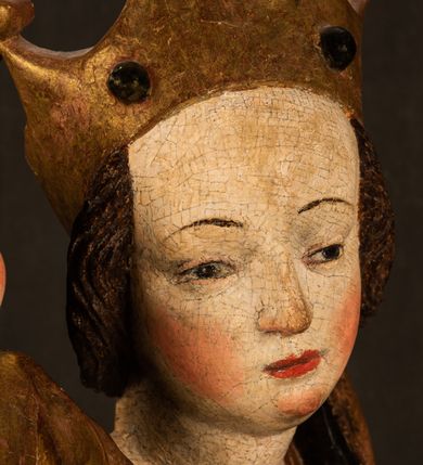 Zdjęcie nr 16: Przyścienna rzeźba Madonny z Dzieciątkiem jest z tyłu wydrążona. W tyle głowy Marii wbity jest hak służący do umocowania w ołtarzu. Matka Boska w całej postaci została ukazana w lekkim kontrapoście z charakterystycznym przegięciem w kształcie odwróconej litery "S". Na prawej ręce trzyma Dzieciątko Jezus, lewą zaś ręką opuszczoną wzdłuż tułowia podtrzymuje nadgarstkiem fałdy płaszcza. Madonna ma pociągłą, zamyśloną twarz o jasnej karnacji, wysokie czoło i pucułowate, rumiane policzki. Ma prosty nos, migdałowe oczy oraz wydatne usta i podbródek. Jej głowę osadzoną na długiej szyi okalają zaczesane do tyłu brązowe włosy, widoczne spod osuwającej się chusty opadającej na ramiona dwoma festonami. Maria ubrana jest w złoconą suknię laserowaną ciepłą czerwienią oraz złocony płaszcz podbity srebrną podszewką z oliwkowo zielonym laserunkiem. Z przodu płaszcz drapowany jest w łukowate fałdy. Jedna z nich biegnie diagonalnie od prawej dłoni ku lewej stopie Madonny. Płaszcz po bokach postaci spływa rurkowatymi kaskadami. Maria na głowię ma wysoką, złotą koronę ze sterczynami o trójlistnych zakończeniach. Mały Jezus został ujęty w trzech czwartych z nieznacznie odchyloną głową do tyłu i skrzyżowanymi nóżkami. Lewą rękę kładzie na piersi matki, w prawej zaś trzyma złocone jabłko. Ma okrągłą, pucułowatą twarz o rumianych policzkach. Charakteryzuje ją prosty nosek, wydatne wargi i podbródek oraz wyraziste, szeroko otwarte oczy. Jego głowę z wysokim czołem okalają krótkie brązowe włosy. Ubrany jest w złocistą długą tunikę odsłaniającą fragmenty stóp.   