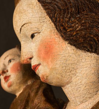 Zdjęcie nr 14: Przyścienna rzeźba Madonny z Dzieciątkiem jest z tyłu wydrążona. W tyle głowy Marii wbity jest hak służący do umocowania w ołtarzu. Matka Boska w całej postaci została ukazana w lekkim kontrapoście z charakterystycznym przegięciem w kształcie odwróconej litery "S". Na prawej ręce trzyma Dzieciątko Jezus, lewą zaś ręką opuszczoną wzdłuż tułowia podtrzymuje nadgarstkiem fałdy płaszcza. Madonna ma pociągłą, zamyśloną twarz o jasnej karnacji, wysokie czoło i pucułowate, rumiane policzki. Ma prosty nos, migdałowe oczy oraz wydatne usta i podbródek. Jej głowę osadzoną na długiej szyi okalają zaczesane do tyłu brązowe włosy, widoczne spod osuwającej się chusty opadającej na ramiona dwoma festonami. Maria ubrana jest w złoconą suknię laserowaną ciepłą czerwienią oraz złocony płaszcz podbity srebrną podszewką z oliwkowo zielonym laserunkiem. Z przodu płaszcz drapowany jest w łukowate fałdy. Jedna z nich biegnie diagonalnie od prawej dłoni ku lewej stopie Madonny. Płaszcz po bokach postaci spływa rurkowatymi kaskadami. Maria na głowię ma wysoką, złotą koronę ze sterczynami o trójlistnych zakończeniach. Mały Jezus został ujęty w trzech czwartych z nieznacznie odchyloną głową do tyłu i skrzyżowanymi nóżkami. Lewą rękę kładzie na piersi matki, w prawej zaś trzyma złocone jabłko. Ma okrągłą, pucułowatą twarz o rumianych policzkach. Charakteryzuje ją prosty nosek, wydatne wargi i podbródek oraz wyraziste, szeroko otwarte oczy. Jego głowę z wysokim czołem okalają krótkie brązowe włosy. Ubrany jest w złocistą długą tunikę odsłaniającą fragmenty stóp.   