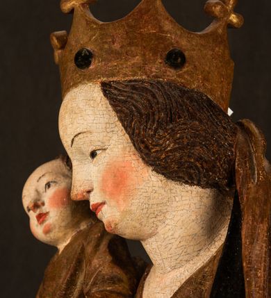 Zdjęcie nr 12: Przyścienna rzeźba Madonny z Dzieciątkiem jest z tyłu wydrążona. W tyle głowy Marii wbity jest hak służący do umocowania w ołtarzu. Matka Boska w całej postaci została ukazana w lekkim kontrapoście z charakterystycznym przegięciem w kształcie odwróconej litery &quot;S&quot;. Na prawej ręce trzyma Dzieciątko Jezus, lewą zaś ręką opuszczoną wzdłuż tułowia podtrzymuje nadgarstkiem fałdy płaszcza. Madonna ma pociągłą, zamyśloną twarz o jasnej karnacji, wysokie czoło i pucułowate, rumiane policzki. Ma prosty nos, migdałowe oczy oraz wydatne usta i podbródek. Jej głowę osadzoną na długiej szyi okalają zaczesane do tyłu brązowe włosy, widoczne spod osuwającej się chusty opadającej na ramiona dwoma festonami. Maria ubrana jest w złoconą suknię laserowaną ciepłą czerwienią oraz złocony płaszcz podbity srebrną podszewką z oliwkowo zielonym laserunkiem. Z przodu płaszcz drapowany jest w łukowate fałdy. Jedna z nich biegnie diagonalnie od prawej dłoni ku lewej stopie Madonny. Płaszcz po bokach postaci spływa rurkowatymi kaskadami. Maria na głowię ma wysoką, złotą koronę ze sterczynami o trójlistnych zakończeniach. Mały Jezus został ujęty w trzech czwartych z nieznacznie odchyloną głową do tyłu i skrzyżowanymi nóżkami. Lewą rękę kładzie na piersi matki, w prawej zaś trzyma złocone jabłko. Ma okrągłą, pucułowatą twarz o rumianych policzkach. Charakteryzuje ją prosty nosek, wydatne wargi i podbródek oraz wyraziste, szeroko otwarte oczy. Jego głowę z wysokim czołem okalają krótkie brązowe włosy. Ubrany jest w złocistą długą tunikę odsłaniającą fragmenty stóp.   