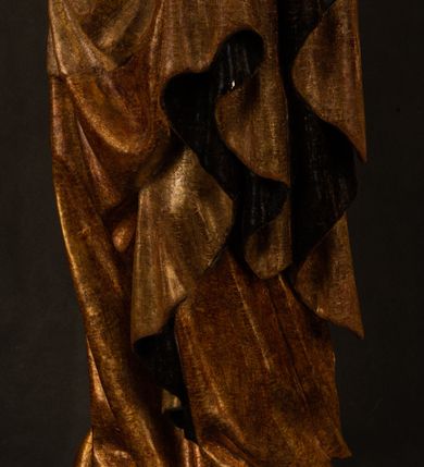 Zdjęcie nr 3: Przyścienna rzeźba Madonny z Dzieciątkiem jest z tyłu wydrążona. W tyle głowy Marii wbity jest hak służący do umocowania w ołtarzu. Matka Boska w całej postaci została ukazana w lekkim kontrapoście z charakterystycznym przegięciem w kształcie odwróconej litery "S". Na prawej ręce trzyma Dzieciątko Jezus, lewą zaś ręką opuszczoną wzdłuż tułowia podtrzymuje nadgarstkiem fałdy płaszcza. Madonna ma pociągłą, zamyśloną twarz o jasnej karnacji, wysokie czoło i pucułowate, rumiane policzki. Ma prosty nos, migdałowe oczy oraz wydatne usta i podbródek. Jej głowę osadzoną na długiej szyi okalają zaczesane do tyłu brązowe włosy, widoczne spod osuwającej się chusty opadającej na ramiona dwoma festonami. Maria ubrana jest w złoconą suknię laserowaną ciepłą czerwienią oraz złocony płaszcz podbity srebrną podszewką z oliwkowo zielonym laserunkiem. Z przodu płaszcz drapowany jest w łukowate fałdy. Jedna z nich biegnie diagonalnie od prawej dłoni ku lewej stopie Madonny. Płaszcz po bokach postaci spływa rurkowatymi kaskadami. Maria na głowię ma wysoką, złotą koronę ze sterczynami o trójlistnych zakończeniach. Mały Jezus został ujęty w trzech czwartych z nieznacznie odchyloną głową do tyłu i skrzyżowanymi nóżkami. Lewą rękę kładzie na piersi matki, w prawej zaś trzyma złocone jabłko. Ma okrągłą, pucułowatą twarz o rumianych policzkach. Charakteryzuje ją prosty nosek, wydatne wargi i podbródek oraz wyraziste, szeroko otwarte oczy. Jego głowę z wysokim czołem okalają krótkie brązowe włosy. Ubrany jest w złocistą długą tunikę odsłaniającą fragmenty stóp.   