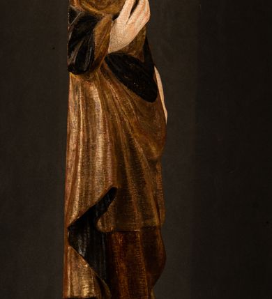 Zdjęcie nr 21: Przyścienna rzeźba Madonny z Dzieciątkiem jest z tyłu wydrążona. W tyle głowy Marii wbity jest hak służący do umocowania w ołtarzu. Matka Boska w całej postaci została ukazana w lekkim kontrapoście z charakterystycznym przegięciem w kształcie odwróconej litery "S". Na prawej ręce trzyma Dzieciątko Jezus, lewą zaś ręką opuszczoną wzdłuż tułowia podtrzymuje nadgarstkiem fałdy płaszcza. Madonna ma pociągłą, zamyśloną twarz o jasnej karnacji, wysokie czoło i pucułowate, rumiane policzki. Ma prosty nos, migdałowe oczy oraz wydatne usta i podbródek. Jej głowę osadzoną na długiej szyi okalają zaczesane do tyłu brązowe włosy, widoczne spod osuwającej się chusty opadającej na ramiona dwoma festonami. Maria ubrana jest w złoconą suknię laserowaną ciepłą czerwienią oraz złocony płaszcz podbity srebrną podszewką z oliwkowo zielonym laserunkiem. Z przodu płaszcz drapowany jest w łukowate fałdy. Jedna z nich biegnie diagonalnie od prawej dłoni ku lewej stopie Madonny. Płaszcz po bokach postaci spływa rurkowatymi kaskadami. Maria na głowię ma wysoką, złotą koronę ze sterczynami o trójlistnych zakończeniach. Mały Jezus został ujęty w trzech czwartych z nieznacznie odchyloną głową do tyłu i skrzyżowanymi nóżkami. Lewą rękę kładzie na piersi matki, w prawej zaś trzyma złocone jabłko. Ma okrągłą, pucułowatą twarz o rumianych policzkach. Charakteryzuje ją prosty nosek, wydatne wargi i podbródek oraz wyraziste, szeroko otwarte oczy. Jego głowę z wysokim czołem okalają krótkie brązowe włosy. Ubrany jest w złocistą długą tunikę odsłaniającą fragmenty stóp.   