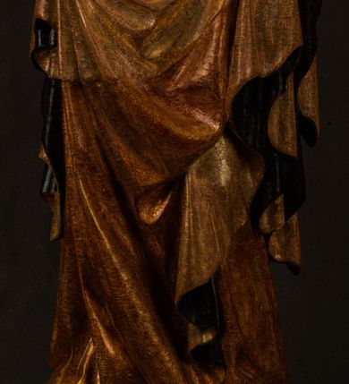 Zdjęcie nr 25: Przyścienna rzeźba Madonny z Dzieciątkiem jest z tyłu wydrążona. W tyle głowy Marii wbity jest hak służący do umocowania w ołtarzu. Matka Boska w całej postaci została ukazana w lekkim kontrapoście z charakterystycznym przegięciem w kształcie odwróconej litery "S". Na prawej ręce trzyma Dzieciątko Jezus, lewą zaś ręką opuszczoną wzdłuż tułowia podtrzymuje nadgarstkiem fałdy płaszcza. Madonna ma pociągłą, zamyśloną twarz o jasnej karnacji, wysokie czoło i pucułowate, rumiane policzki. Ma prosty nos, migdałowe oczy oraz wydatne usta i podbródek. Jej głowę osadzoną na długiej szyi okalają zaczesane do tyłu brązowe włosy, widoczne spod osuwającej się chusty opadającej na ramiona dwoma festonami. Maria ubrana jest w złoconą suknię laserowaną ciepłą czerwienią oraz złocony płaszcz podbity srebrną podszewką z oliwkowo zielonym laserunkiem. Z przodu płaszcz drapowany jest w łukowate fałdy. Jedna z nich biegnie diagonalnie od prawej dłoni ku lewej stopie Madonny. Płaszcz po bokach postaci spływa rurkowatymi kaskadami. Maria na głowię ma wysoką, złotą koronę ze sterczynami o trójlistnych zakończeniach. Mały Jezus został ujęty w trzech czwartych z nieznacznie odchyloną głową do tyłu i skrzyżowanymi nóżkami. Lewą rękę kładzie na piersi matki, w prawej zaś trzyma złocone jabłko. Ma okrągłą, pucułowatą twarz o rumianych policzkach. Charakteryzuje ją prosty nosek, wydatne wargi i podbródek oraz wyraziste, szeroko otwarte oczy. Jego głowę z wysokim czołem okalają krótkie brązowe włosy. Ubrany jest w złocistą długą tunikę odsłaniającą fragmenty stóp.   