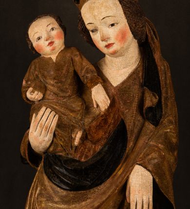 Zdjęcie nr 5: Przyścienna rzeźba Madonny z Dzieciątkiem jest z tyłu wydrążona. W tyle głowy Marii wbity jest hak służący do umocowania w ołtarzu. Matka Boska w całej postaci została ukazana w lekkim kontrapoście z charakterystycznym przegięciem w kształcie odwróconej litery "S". Na prawej ręce trzyma Dzieciątko Jezus, lewą zaś ręką opuszczoną wzdłuż tułowia podtrzymuje nadgarstkiem fałdy płaszcza. Madonna ma pociągłą, zamyśloną twarz o jasnej karnacji, wysokie czoło i pucułowate, rumiane policzki. Ma prosty nos, migdałowe oczy oraz wydatne usta i podbródek. Jej głowę osadzoną na długiej szyi okalają zaczesane do tyłu brązowe włosy, widoczne spod osuwającej się chusty opadającej na ramiona dwoma festonami. Maria ubrana jest w złoconą suknię laserowaną ciepłą czerwienią oraz złocony płaszcz podbity srebrną podszewką z oliwkowo zielonym laserunkiem. Z przodu płaszcz drapowany jest w łukowate fałdy. Jedna z nich biegnie diagonalnie od prawej dłoni ku lewej stopie Madonny. Płaszcz po bokach postaci spływa rurkowatymi kaskadami. Maria na głowię ma wysoką, złotą koronę ze sterczynami o trójlistnych zakończeniach. Mały Jezus został ujęty w trzech czwartych z nieznacznie odchyloną głową do tyłu i skrzyżowanymi nóżkami. Lewą rękę kładzie na piersi matki, w prawej zaś trzyma złocone jabłko. Ma okrągłą, pucułowatą twarz o rumianych policzkach. Charakteryzuje ją prosty nosek, wydatne wargi i podbródek oraz wyraziste, szeroko otwarte oczy. Jego głowę z wysokim czołem okalają krótkie brązowe włosy. Ubrany jest w złocistą długą tunikę odsłaniającą fragmenty stóp.   