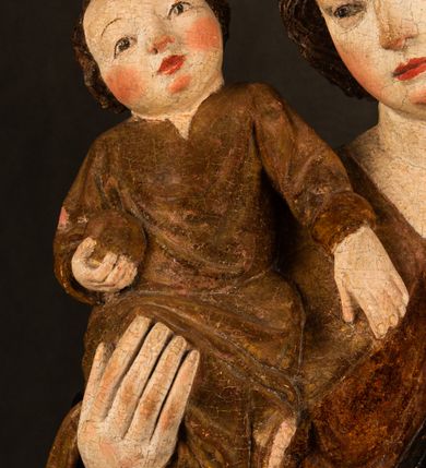 Zdjęcie nr 9: Przyścienna rzeźba Madonny z Dzieciątkiem jest z tyłu wydrążona. W tyle głowy Marii wbity jest hak służący do umocowania w ołtarzu. Matka Boska w całej postaci została ukazana w lekkim kontrapoście z charakterystycznym przegięciem w kształcie odwróconej litery "S". Na prawej ręce trzyma Dzieciątko Jezus, lewą zaś ręką opuszczoną wzdłuż tułowia podtrzymuje nadgarstkiem fałdy płaszcza. Madonna ma pociągłą, zamyśloną twarz o jasnej karnacji, wysokie czoło i pucułowate, rumiane policzki. Ma prosty nos, migdałowe oczy oraz wydatne usta i podbródek. Jej głowę osadzoną na długiej szyi okalają zaczesane do tyłu brązowe włosy, widoczne spod osuwającej się chusty opadającej na ramiona dwoma festonami. Maria ubrana jest w złoconą suknię laserowaną ciepłą czerwienią oraz złocony płaszcz podbity srebrną podszewką z oliwkowo zielonym laserunkiem. Z przodu płaszcz drapowany jest w łukowate fałdy. Jedna z nich biegnie diagonalnie od prawej dłoni ku lewej stopie Madonny. Płaszcz po bokach postaci spływa rurkowatymi kaskadami. Maria na głowię ma wysoką, złotą koronę ze sterczynami o trójlistnych zakończeniach. Mały Jezus został ujęty w trzech czwartych z nieznacznie odchyloną głową do tyłu i skrzyżowanymi nóżkami. Lewą rękę kładzie na piersi matki, w prawej zaś trzyma złocone jabłko. Ma okrągłą, pucułowatą twarz o rumianych policzkach. Charakteryzuje ją prosty nosek, wydatne wargi i podbródek oraz wyraziste, szeroko otwarte oczy. Jego głowę z wysokim czołem okalają krótkie brązowe włosy. Ubrany jest w złocistą długą tunikę odsłaniającą fragmenty stóp.   