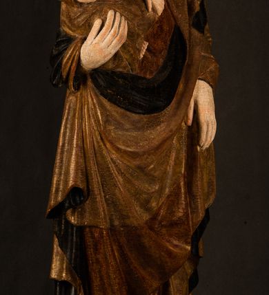 Zdjęcie nr 2: Przyścienna rzeźba Madonny z Dzieciątkiem jest z tyłu wydrążona. W tyle głowy Marii wbity jest hak służący do umocowania w ołtarzu. Matka Boska w całej postaci została ukazana w lekkim kontrapoście z charakterystycznym przegięciem w kształcie odwróconej litery "S". Na prawej ręce trzyma Dzieciątko Jezus, lewą zaś ręką opuszczoną wzdłuż tułowia podtrzymuje nadgarstkiem fałdy płaszcza. Madonna ma pociągłą, zamyśloną twarz o jasnej karnacji, wysokie czoło i pucułowate, rumiane policzki. Ma prosty nos, migdałowe oczy oraz wydatne usta i podbródek. Jej głowę osadzoną na długiej szyi okalają zaczesane do tyłu brązowe włosy, widoczne spod osuwającej się chusty opadającej na ramiona dwoma festonami. Maria ubrana jest w złoconą suknię laserowaną ciepłą czerwienią oraz złocony płaszcz podbity srebrną podszewką z oliwkowo zielonym laserunkiem. Z przodu płaszcz drapowany jest w łukowate fałdy. Jedna z nich biegnie diagonalnie od prawej dłoni ku lewej stopie Madonny. Płaszcz po bokach postaci spływa rurkowatymi kaskadami. Maria na głowię ma wysoką, złotą koronę ze sterczynami o trójlistnych zakończeniach. Mały Jezus został ujęty w trzech czwartych z nieznacznie odchyloną głową do tyłu i skrzyżowanymi nóżkami. Lewą rękę kładzie na piersi matki, w prawej zaś trzyma złocone jabłko. Ma okrągłą, pucułowatą twarz o rumianych policzkach. Charakteryzuje ją prosty nosek, wydatne wargi i podbródek oraz wyraziste, szeroko otwarte oczy. Jego głowę z wysokim czołem okalają krótkie brązowe włosy. Ubrany jest w złocistą długą tunikę odsłaniającą fragmenty stóp.   