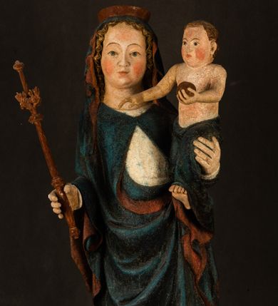 Zdjęcie nr 1: Rzeźba drążona, ukazująca Matkę Boską z Dzieciątkiem. Maria ustawiona frontalnie, w delikatnym kontrapoście, na lewym ręku trzyma Dzieciątko, w prawym dzierży berło. Twarz okrągła z wysokim czołem, drobnymi ustami i małymi oczami o delikatnie zarysowanych łukach brwiowych. Włosy jasne, ułożone w skręcone pukle spływające na plecy. Maria ubrana jest w białą suknię zdobioną drobnymi, niebieskimi gwiazdkami, ciemnobłękitny płaszcz z bordową podszewką spięty na piersi oraz spiczaste, brązowe buty. Na głowie ma założony ciemnoniebieski welon z bordową podszewką, spływający na ramiona i piersi oraz brązową podstawę do niezachowanej korony. Draperia szat miękka o wyraźnie zaznaczonych, licznych fałdach misowych i kaskadowych. Dzieciątko ukazane w pozycji siedzącej, zwrócone w prawo. W lewej dłoni trzyma jabłko królewskie, a prawą wyprostowaną podnosi na wysokość tułowia. Twarz pełna o dziecięcych rysach z małymi ustami, okolona krótkimi i kędzierzawymi włosami. Polichromia w odsłoniętych partiach ciała naturalistyczna, berło polichromowane na brązowo.