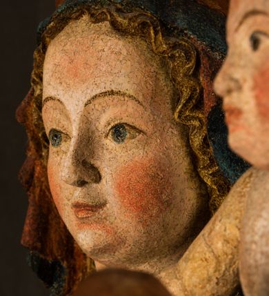 Zdjęcie nr 16: Rzeźba drążona, ukazująca Matkę Boską z Dzieciątkiem. Maria ustawiona frontalnie, w delikatnym kontrapoście, na lewym ręku trzyma Dzieciątko, w prawym dzierży berło. Twarz okrągła z wysokim czołem, drobnymi ustami i małymi oczami o delikatnie zarysowanych łukach brwiowych. Włosy jasne, ułożone w skręcone pukle spływające na plecy. Maria ubrana jest w białą suknię zdobioną drobnymi, niebieskimi gwiazdkami, ciemnobłękitny płaszcz z bordową podszewką spięty na piersi oraz spiczaste, brązowe buty. Na głowie ma założony ciemnoniebieski welon z bordową podszewką, spływający na ramiona i piersi oraz brązową podstawę do niezachowanej korony. Draperia szat miękka o wyraźnie zaznaczonych, licznych fałdach misowych i kaskadowych. Dzieciątko ukazane w pozycji siedzącej, zwrócone w prawo. W lewej dłoni trzyma jabłko królewskie, a prawą wyprostowaną podnosi na wysokość tułowia. Twarz pełna o dziecięcych rysach z małymi ustami, okolona krótkimi i kędzierzawymi włosami. Polichromia w odsłoniętych partiach ciała naturalistyczna, berło polichromowane na brązowo.