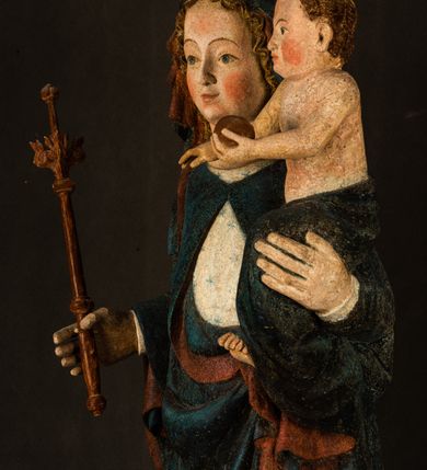 Zdjęcie nr 4: Rzeźba drążona, ukazująca Matkę Boską z Dzieciątkiem. Maria ustawiona frontalnie, w delikatnym kontrapoście, na lewym ręku trzyma Dzieciątko, w prawym dzierży berło. Twarz okrągła z wysokim czołem, drobnymi ustami i małymi oczami o delikatnie zarysowanych łukach brwiowych. Włosy jasne, ułożone w skręcone pukle spływające na plecy. Maria ubrana jest w białą suknię zdobioną drobnymi, niebieskimi gwiazdkami, ciemnobłękitny płaszcz z bordową podszewką spięty na piersi oraz spiczaste, brązowe buty. Na głowie ma założony ciemnoniebieski welon z bordową podszewką, spływający na ramiona i piersi oraz brązową podstawę do niezachowanej korony. Draperia szat miękka o wyraźnie zaznaczonych, licznych fałdach misowych i kaskadowych. Dzieciątko ukazane w pozycji siedzącej, zwrócone w prawo. W lewej dłoni trzyma jabłko królewskie, a prawą wyprostowaną podnosi na wysokość tułowia. Twarz pełna o dziecięcych rysach z małymi ustami, okolona krótkimi i kędzierzawymi włosami. Polichromia w odsłoniętych partiach ciała naturalistyczna, berło polichromowane na brązowo.