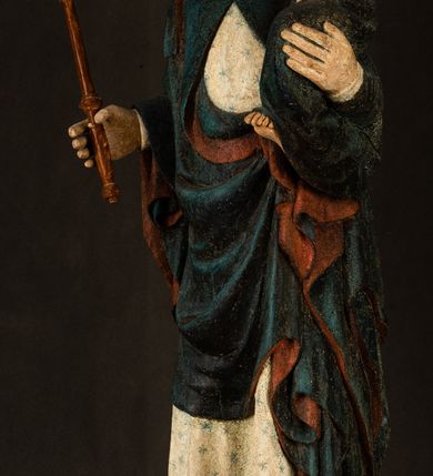 Zdjęcie nr 2: Rzeźba drążona, ukazująca Matkę Boską z Dzieciątkiem. Maria ustawiona frontalnie, w delikatnym kontrapoście, na lewym ręku trzyma Dzieciątko, w prawym dzierży berło. Twarz okrągła z wysokim czołem, drobnymi ustami i małymi oczami o delikatnie zarysowanych łukach brwiowych. Włosy jasne, ułożone w skręcone pukle spływające na plecy. Maria ubrana jest w białą suknię zdobioną drobnymi, niebieskimi gwiazdkami, ciemnobłękitny płaszcz z bordową podszewką spięty na piersi oraz spiczaste, brązowe buty. Na głowie ma założony ciemnoniebieski welon z bordową podszewką, spływający na ramiona i piersi oraz brązową podstawę do niezachowanej korony. Draperia szat miękka o wyraźnie zaznaczonych, licznych fałdach misowych i kaskadowych. Dzieciątko ukazane w pozycji siedzącej, zwrócone w prawo. W lewej dłoni trzyma jabłko królewskie, a prawą wyprostowaną podnosi na wysokość tułowia. Twarz pełna o dziecięcych rysach z małymi ustami, okolona krótkimi i kędzierzawymi włosami. Polichromia w odsłoniętych partiach ciała naturalistyczna, berło polichromowane na brązowo.