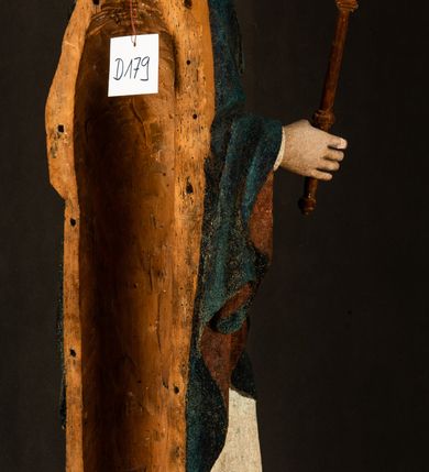 Zdjęcie nr 20: Rzeźba drążona, ukazująca Matkę Boską z Dzieciątkiem. Maria ustawiona frontalnie, w delikatnym kontrapoście, na lewym ręku trzyma Dzieciątko, w prawym dzierży berło. Twarz okrągła z wysokim czołem, drobnymi ustami i małymi oczami o delikatnie zarysowanych łukach brwiowych. Włosy jasne, ułożone w skręcone pukle spływające na plecy. Maria ubrana jest w białą suknię zdobioną drobnymi, niebieskimi gwiazdkami, ciemnobłękitny płaszcz z bordową podszewką spięty na piersi oraz spiczaste, brązowe buty. Na głowie ma założony ciemnoniebieski welon z bordową podszewką, spływający na ramiona i piersi oraz brązową podstawę do niezachowanej korony. Draperia szat miękka o wyraźnie zaznaczonych, licznych fałdach misowych i kaskadowych. Dzieciątko ukazane w pozycji siedzącej, zwrócone w prawo. W lewej dłoni trzyma jabłko królewskie, a prawą wyprostowaną podnosi na wysokość tułowia. Twarz pełna o dziecięcych rysach z małymi ustami, okolona krótkimi i kędzierzawymi włosami. Polichromia w odsłoniętych partiach ciała naturalistyczna, berło polichromowane na brązowo.